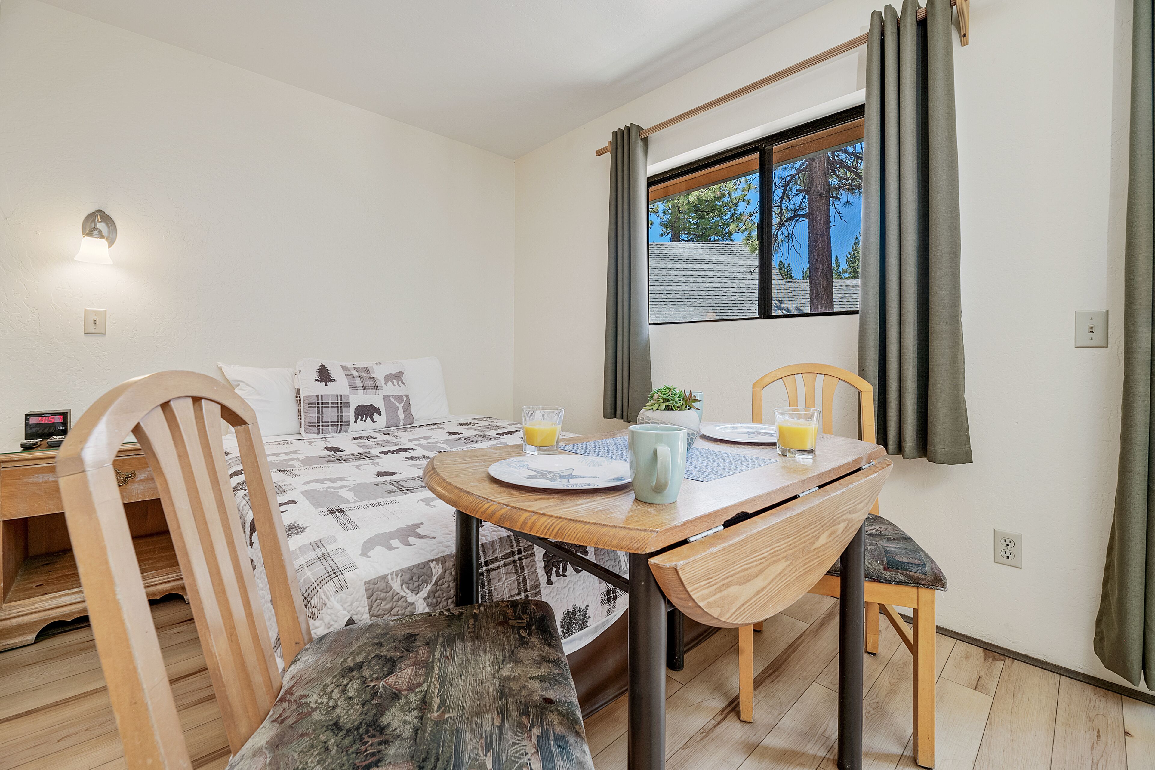 Una habitación pequeña y acogedora con una cama, una mesa de madera y una ventana con cortinas.