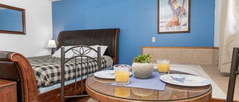 A bedroom with a bed, a dining table with breakfast items, and a poster on the wall.