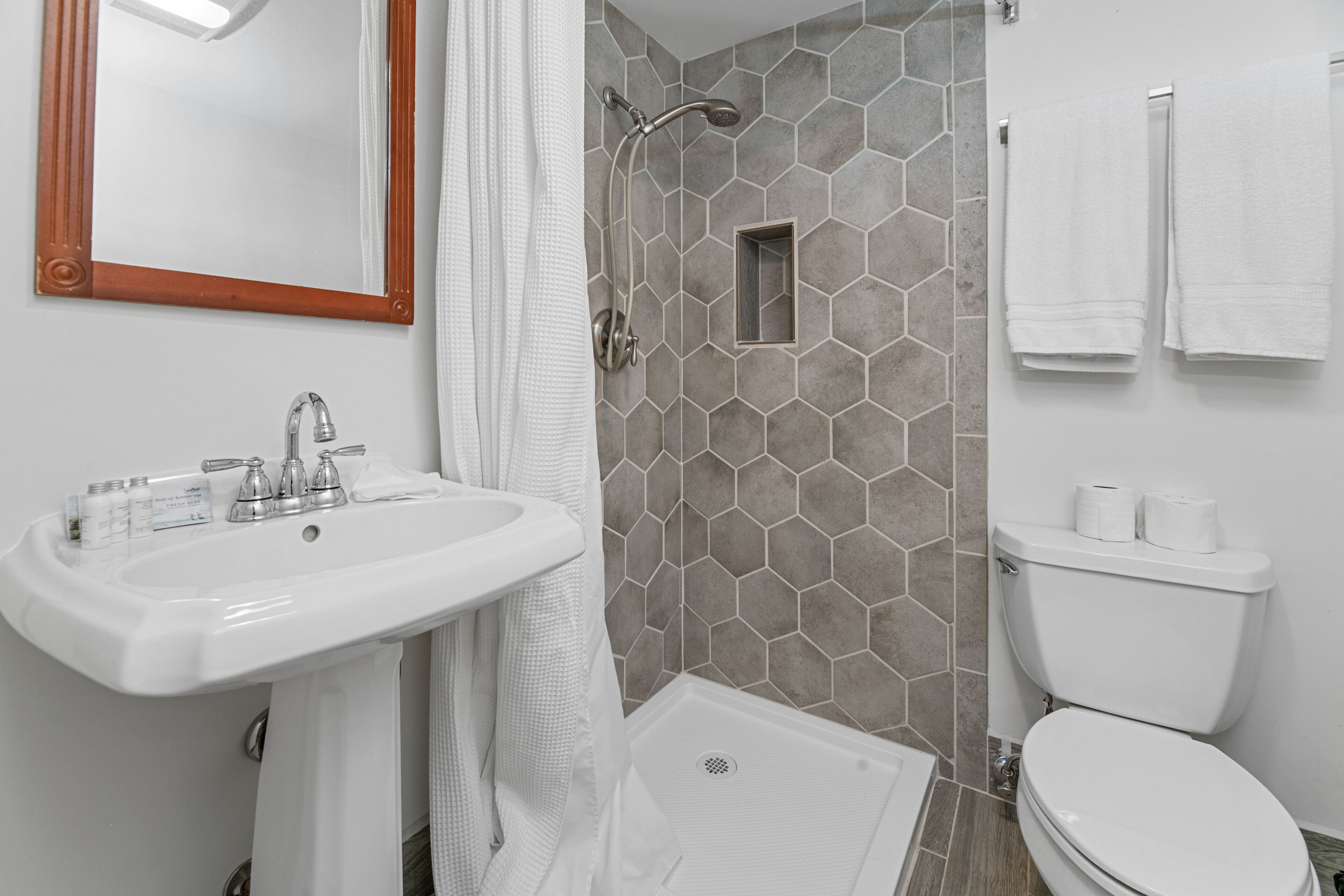 A bathroom with a white sink, a shower with a hexagonal tile wall, and a toilet.