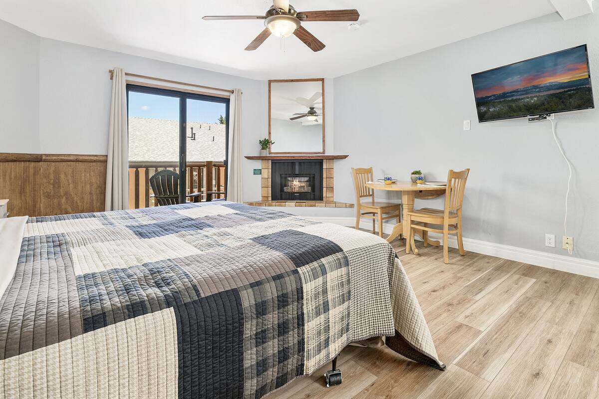 Ein Schlafzimmer mit einem großen Bett, einem Kamin, einem Esstisch mit Stühlen, einem an der Wand befestigten Fernseher und einem Balkon mit Aussicht.