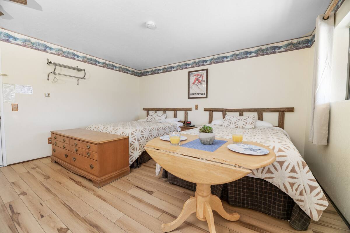 Ein Schlafzimmer mit zwei Betten, einer Holzkommode, einem kleinen Tisch mit Tablett und einem Poster an der Wand.