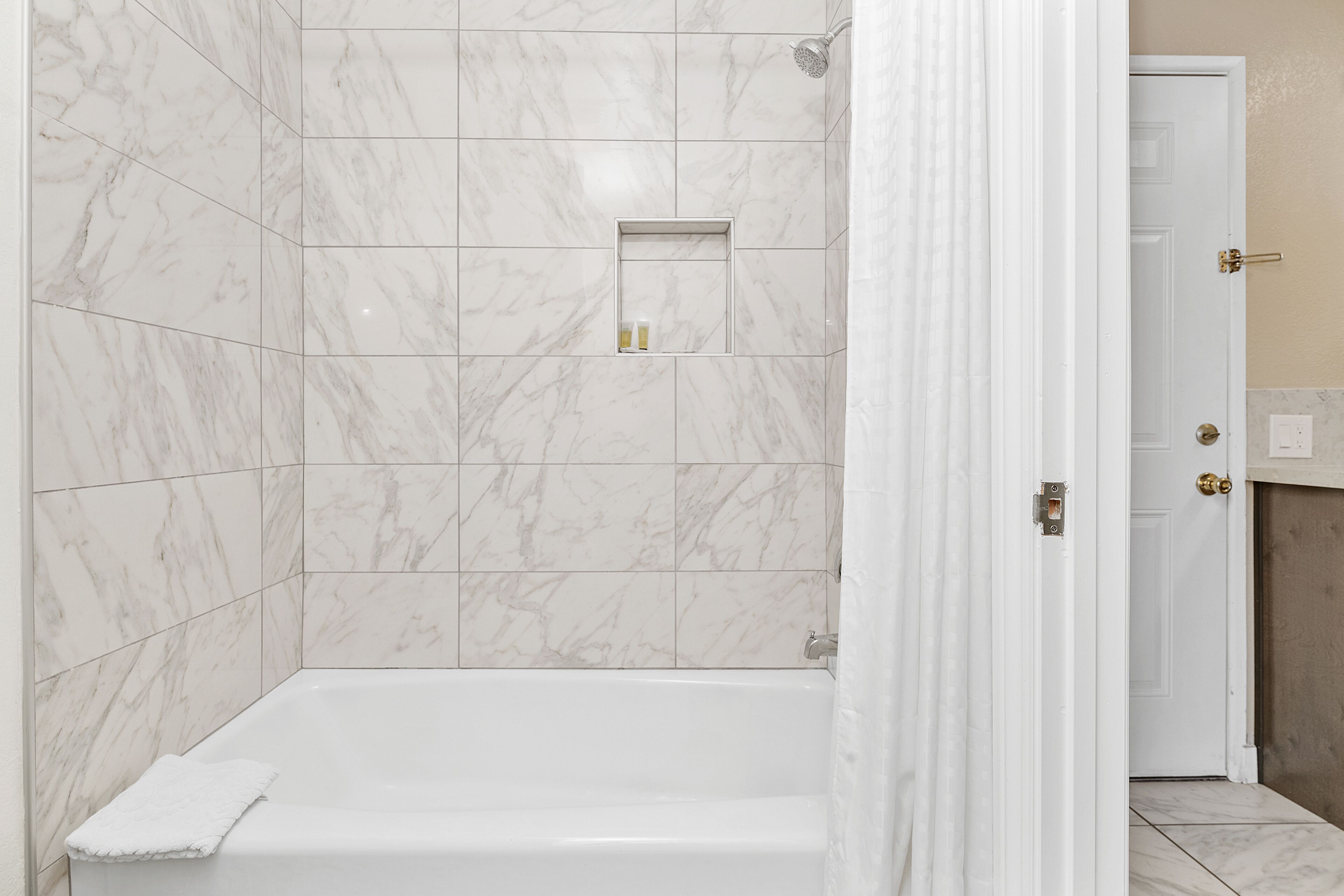 Une salle de bain avec une baignoire blanche, des carreaux de marbre, un espace douche et une petite étagère contenant des articles de toilette.
