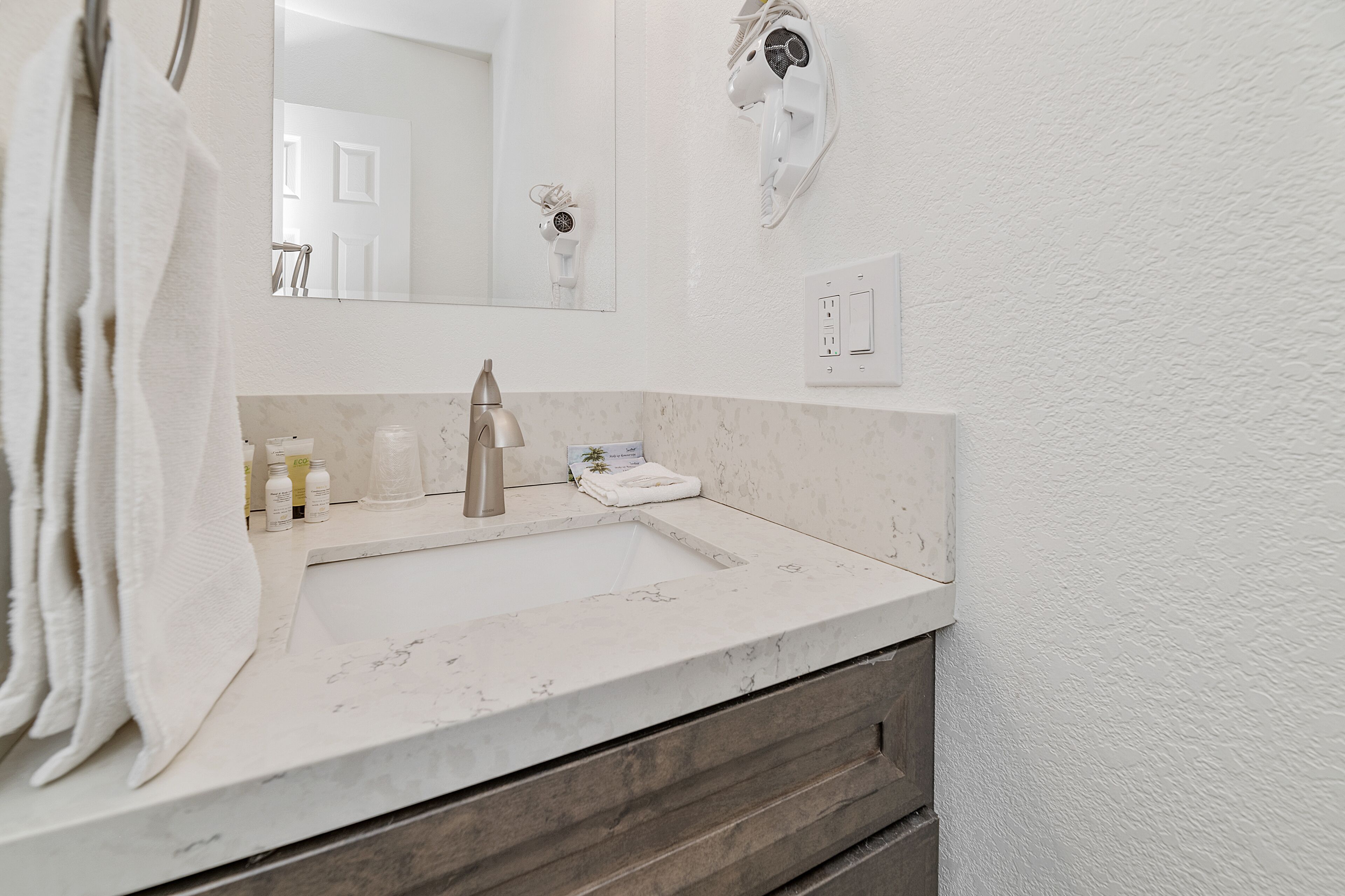 A bathroom with a marble sink, a towel rack, a hairdryer mounted on the wall, and a mirror.