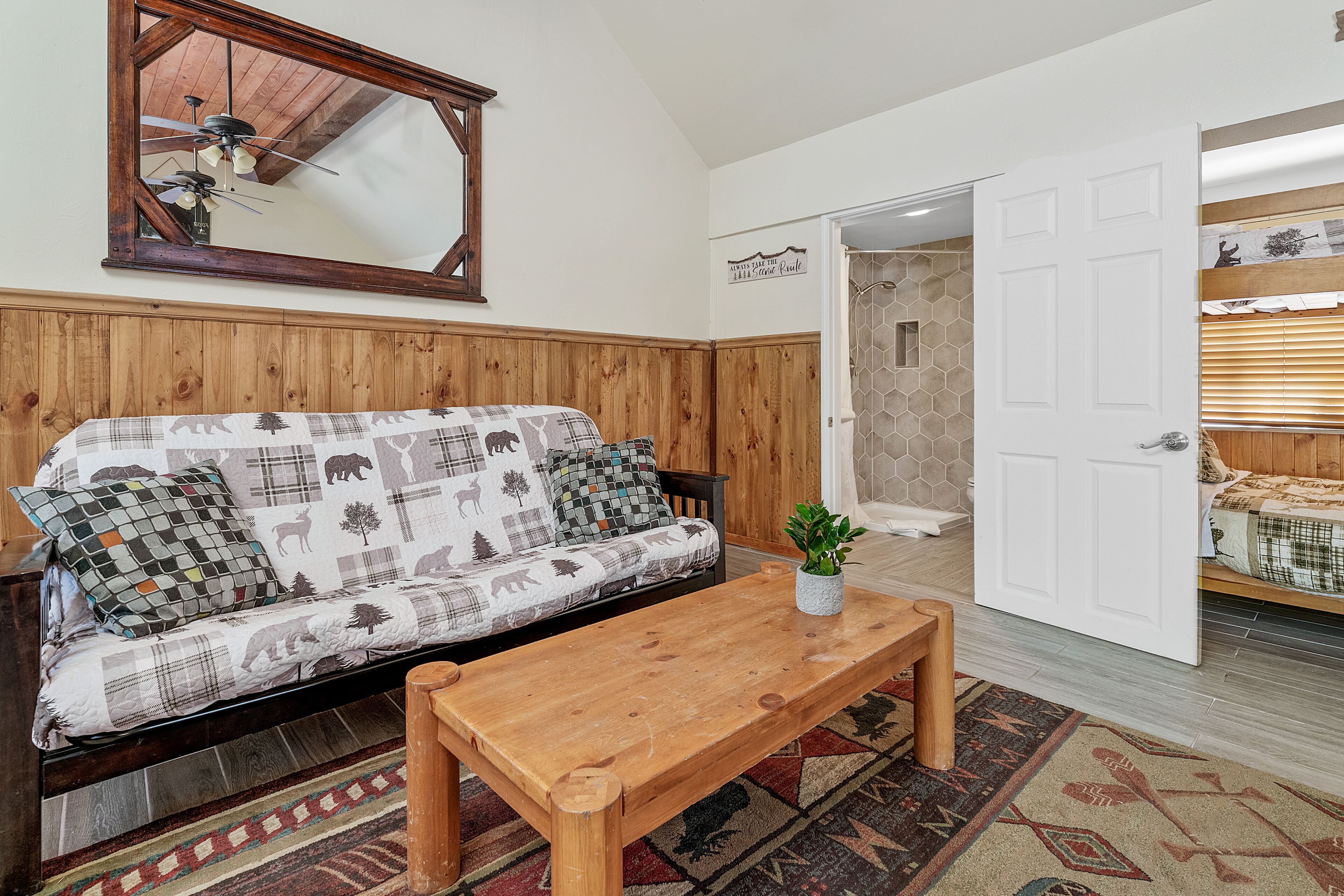 A room with a wooden panel wall, a sofa with patterned cushions, a wooden coffee table, and a mirror above the sofa.