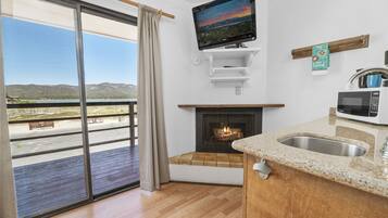 Eine moderne Küche mit Kamin, einem darüber angebrachten Fernseher und Blick auf einen Balkon mit einer schönen Landschaft.