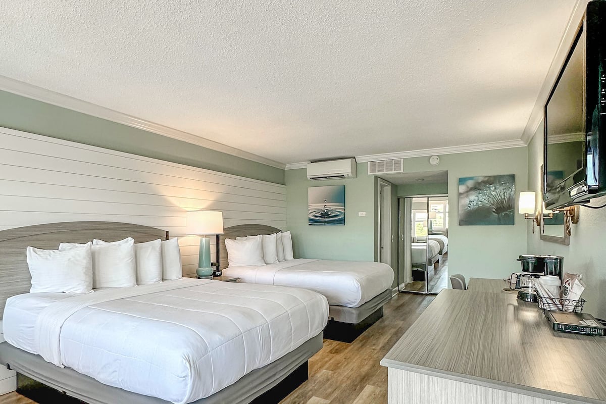 Une chambre d’hôtel avec deux lits, un plancher en bois, un bureau avec une lampe et un téléviseur.