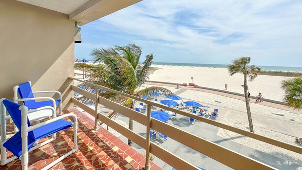 A balcony with a view of a beach, featuring blue lounge chairs and a tiled floor.