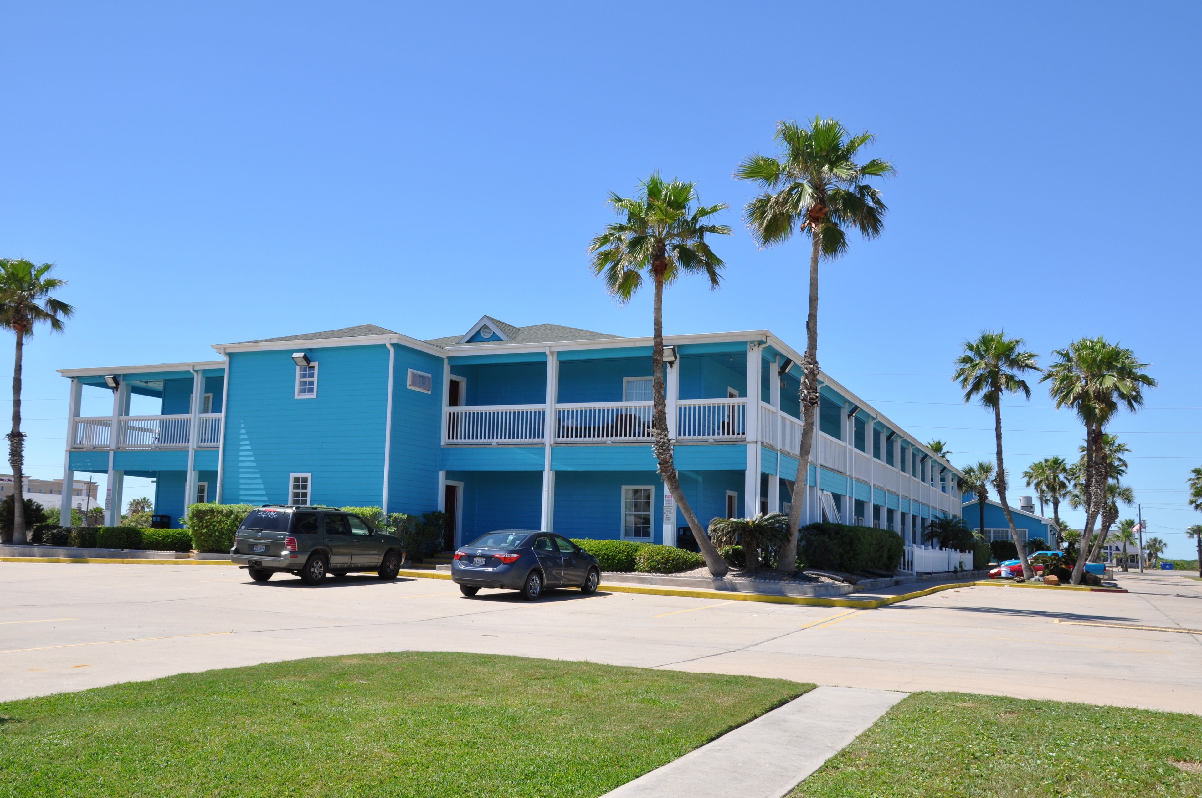 A two-story hotel with a blue exterior, multiple balconies, and palm trees in the foreground.