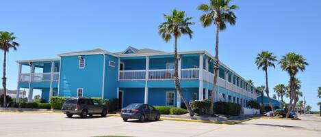 A two-story hotel with a blue exterior, multiple balconies, and palm trees in the foreground.