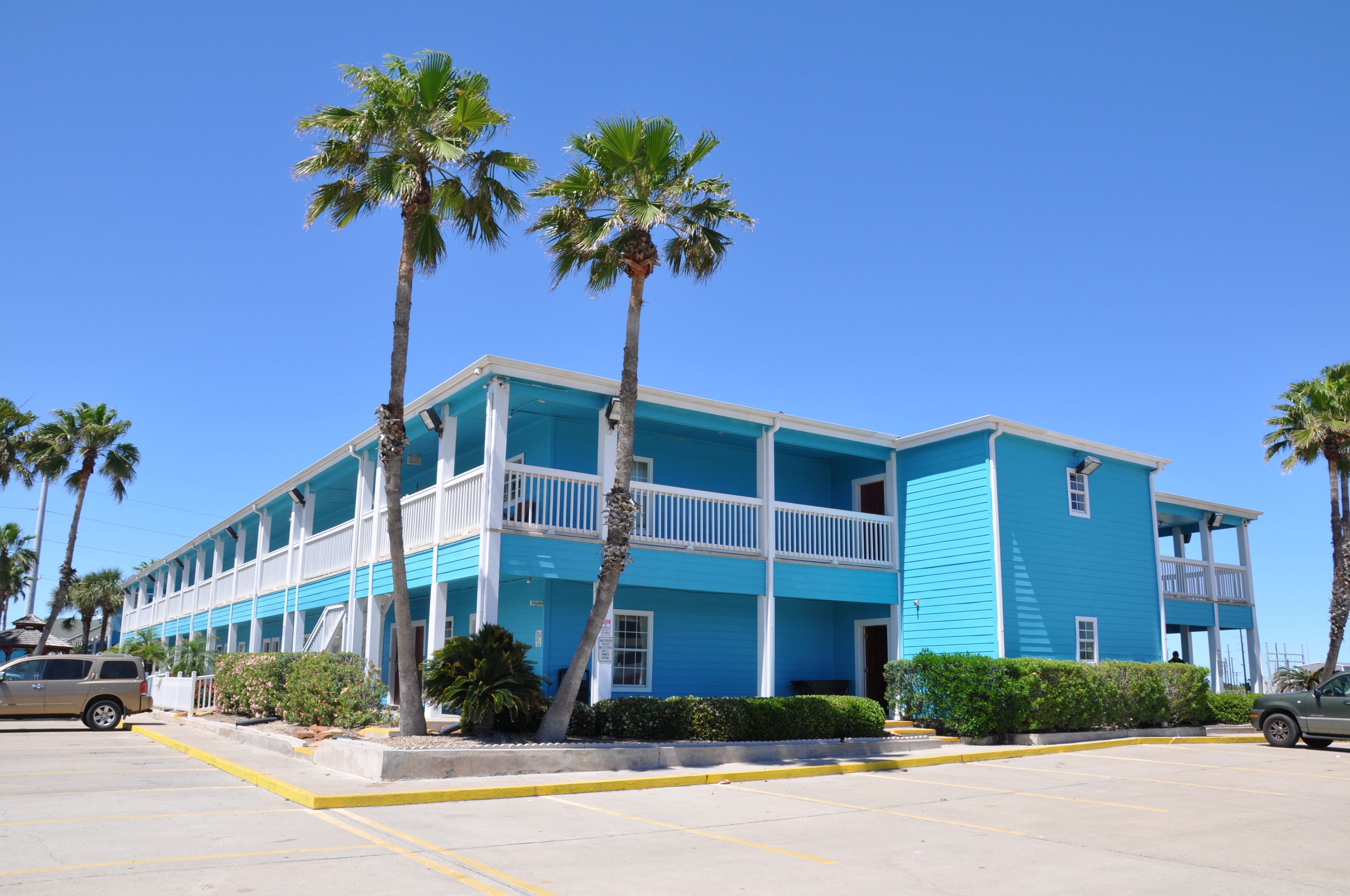 A two-story motel with a blue exterior, multiple balconies, and palm trees in the foreground.