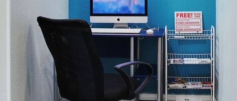 A corner office with a desk, computer, and a chair. There is a blue wall with a white ring light and a sign offering free newspapers.