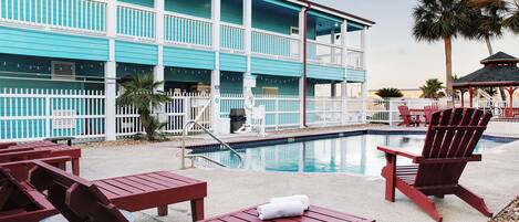 A poolside area with red Adirondack chairs and a pool.