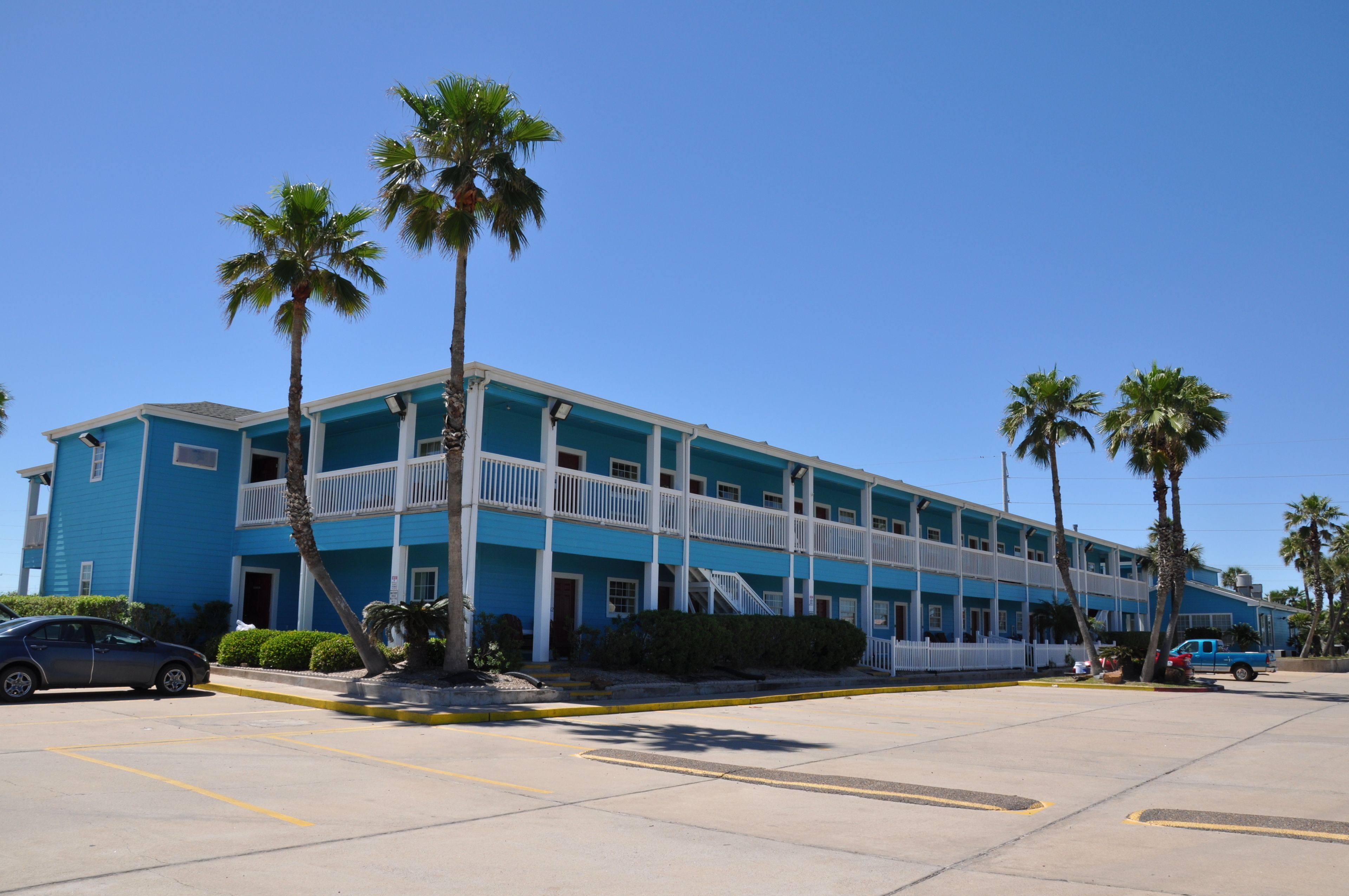 A two-story motel with a blue exterior, white balconies, and palm trees in the parking lot.