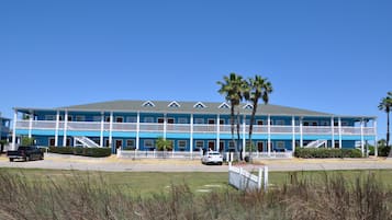 A two-story motel with a blue exterior and white railings, featuring a central staircase, palm trees, and a parking lot.