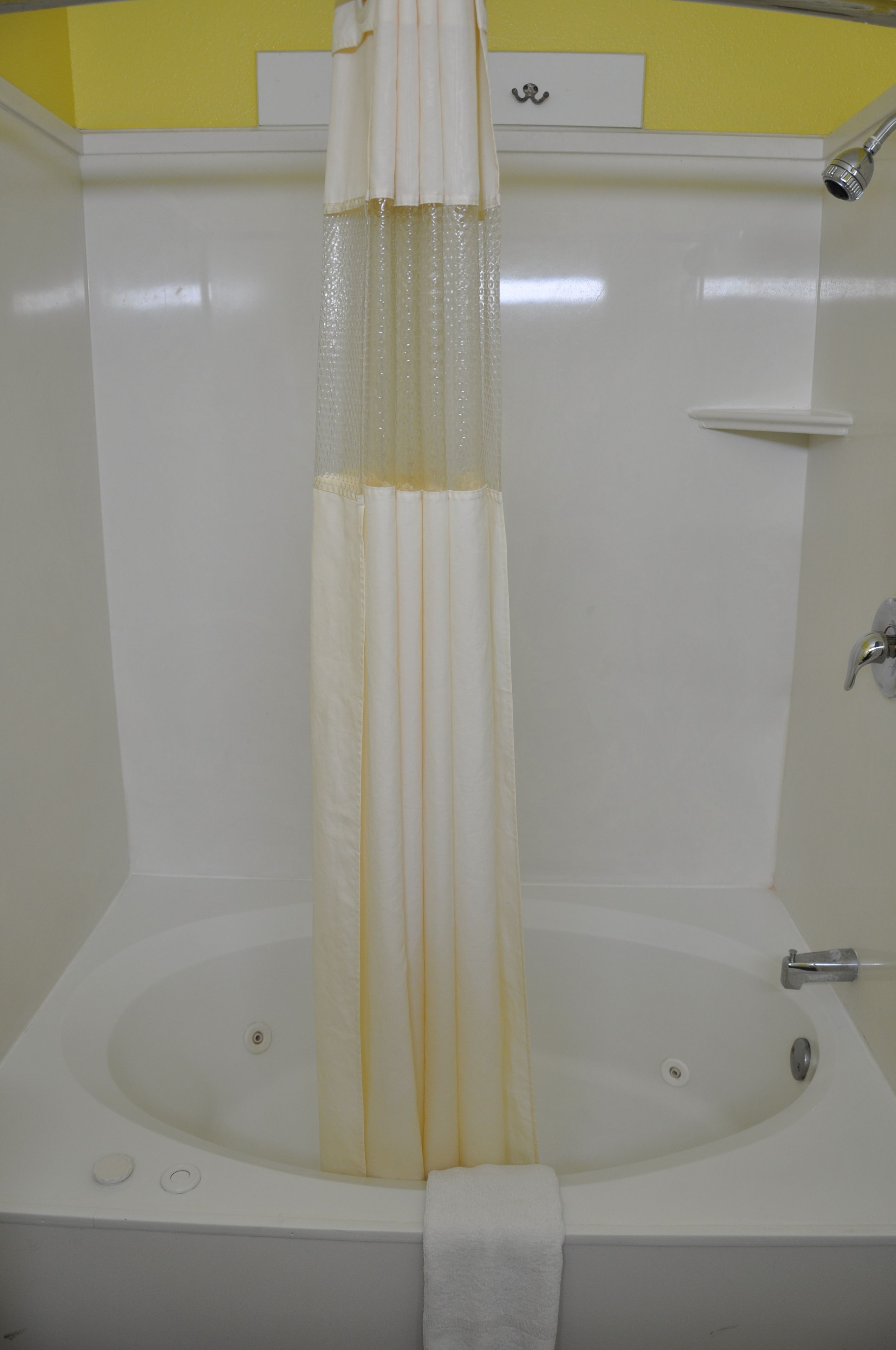 A white bathtub with a shower curtain, a towel, and a small shelf.