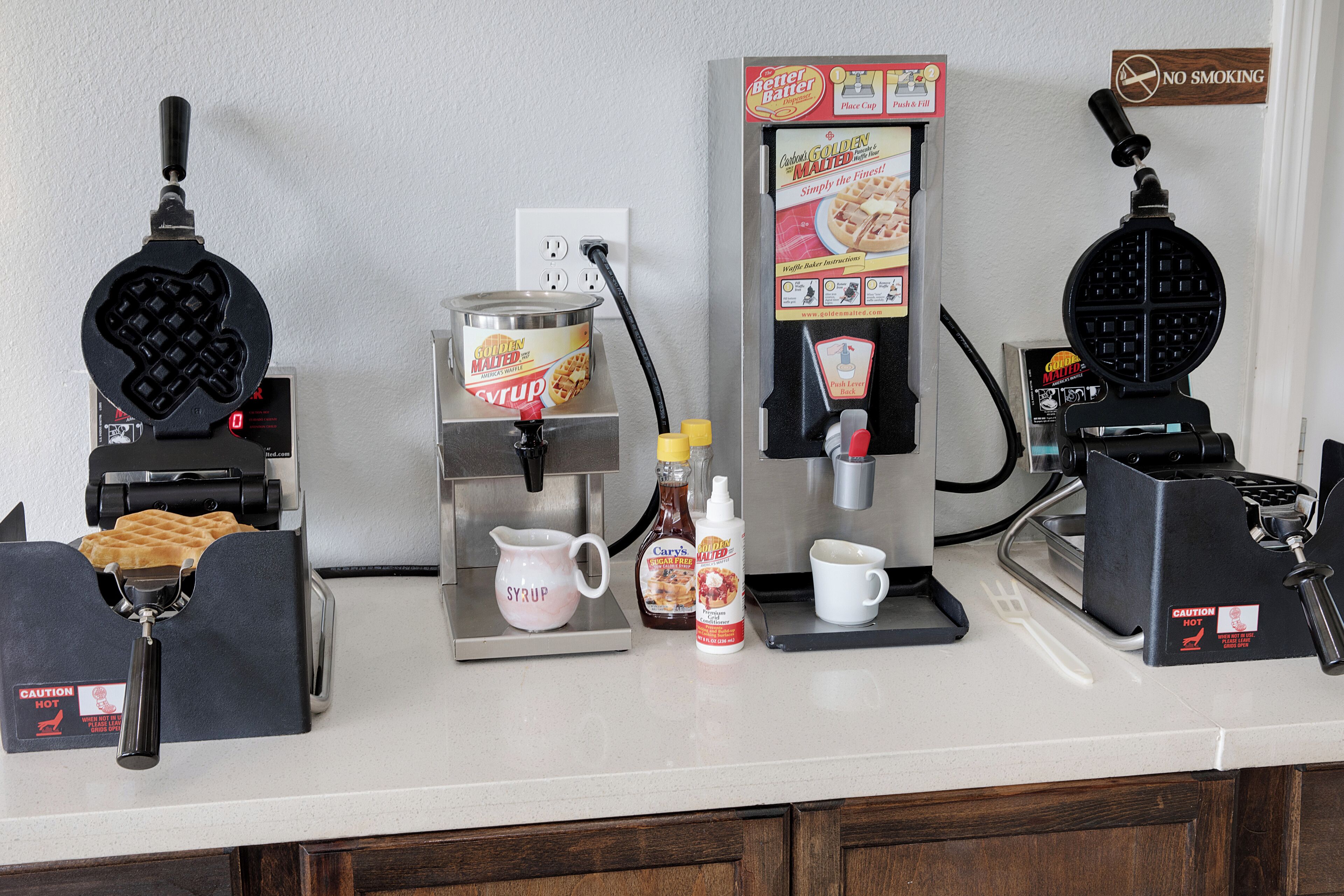 Una encimera de cocina con máquinas para hacer gofres, jarabe y una cafetera.