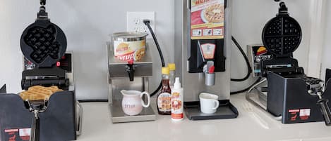 A kitchen counter with waffle makers, syrup, and a coffee machine.