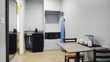Cocina compacta con lavamanos, microondas y refrigerador pequeño. Hay una mesa de comedor con sillas y una bandeja con tazas.