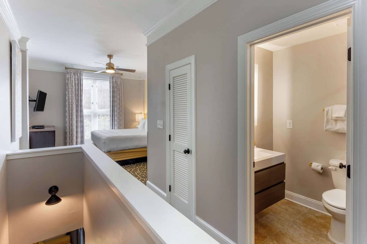 Ein Hotelzimmer mit Bett, Deckenventilator, Bad mit Toilette und Waschbecken sowie einem kleinen Schreibtisch mit Lampe.