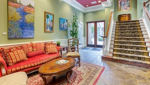 A spacious living area with a red sofa, a wooden coffee table, and a staircase with ornate carpet. - Church Street Inn Historic Charleston, Ascend Collection Hotel (Charleston)