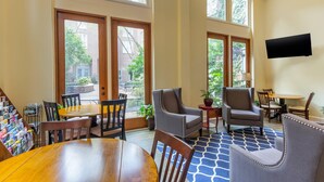 A spacious indoor area with a wooden table and chairs, a blue patterned rug, and large windows offering a view of the outside. - Church Street Inn Historic Charleston, Ascend Collection Hotel (Charleston)