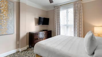 A hotel room with a bed, a flat-screen TV mounted on the wall, a dresser, and a window with curtains.