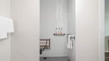 Un box de ducha estrecho, con azulejos blancos, un perchero y un estante con artículos de aseo.