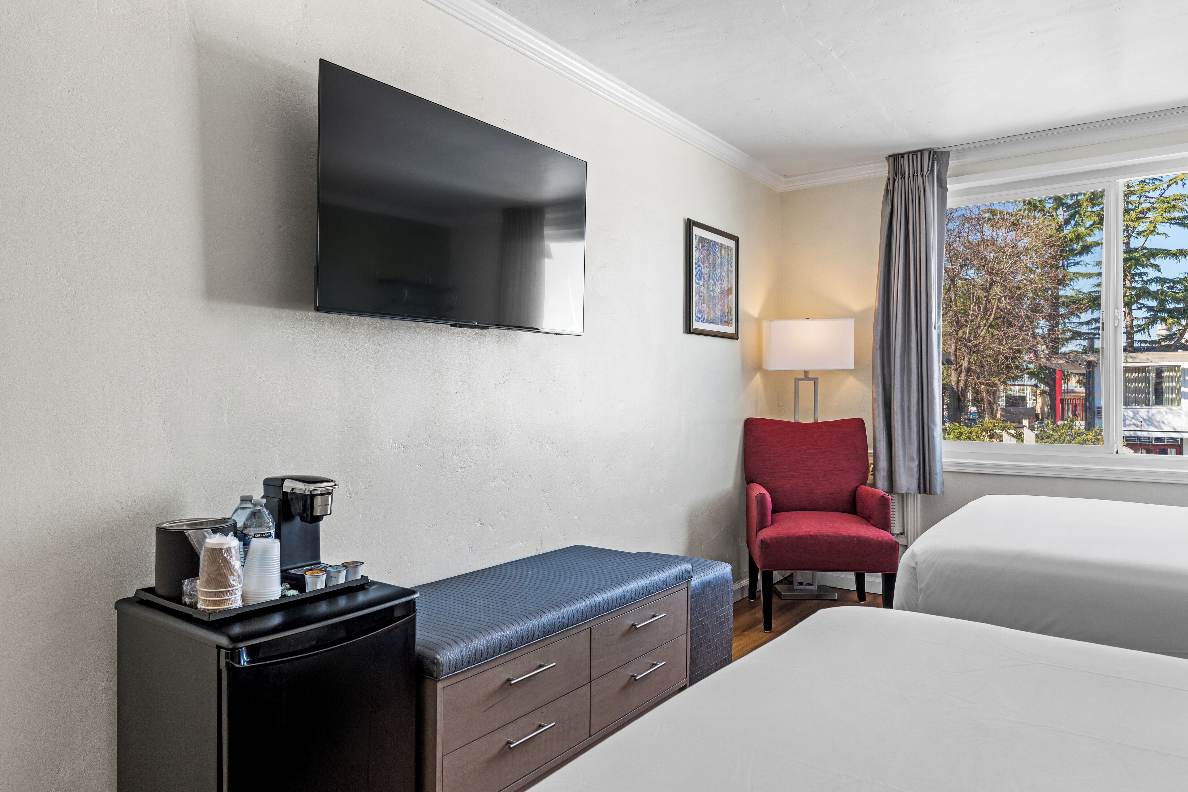 Hotelkamer met flatscreen televisie, koffieapparaat, rode stoel en bed.