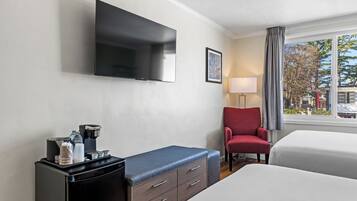 Hotelkamer met flatscreen televisie, koffieapparaat, rode stoel en bed.