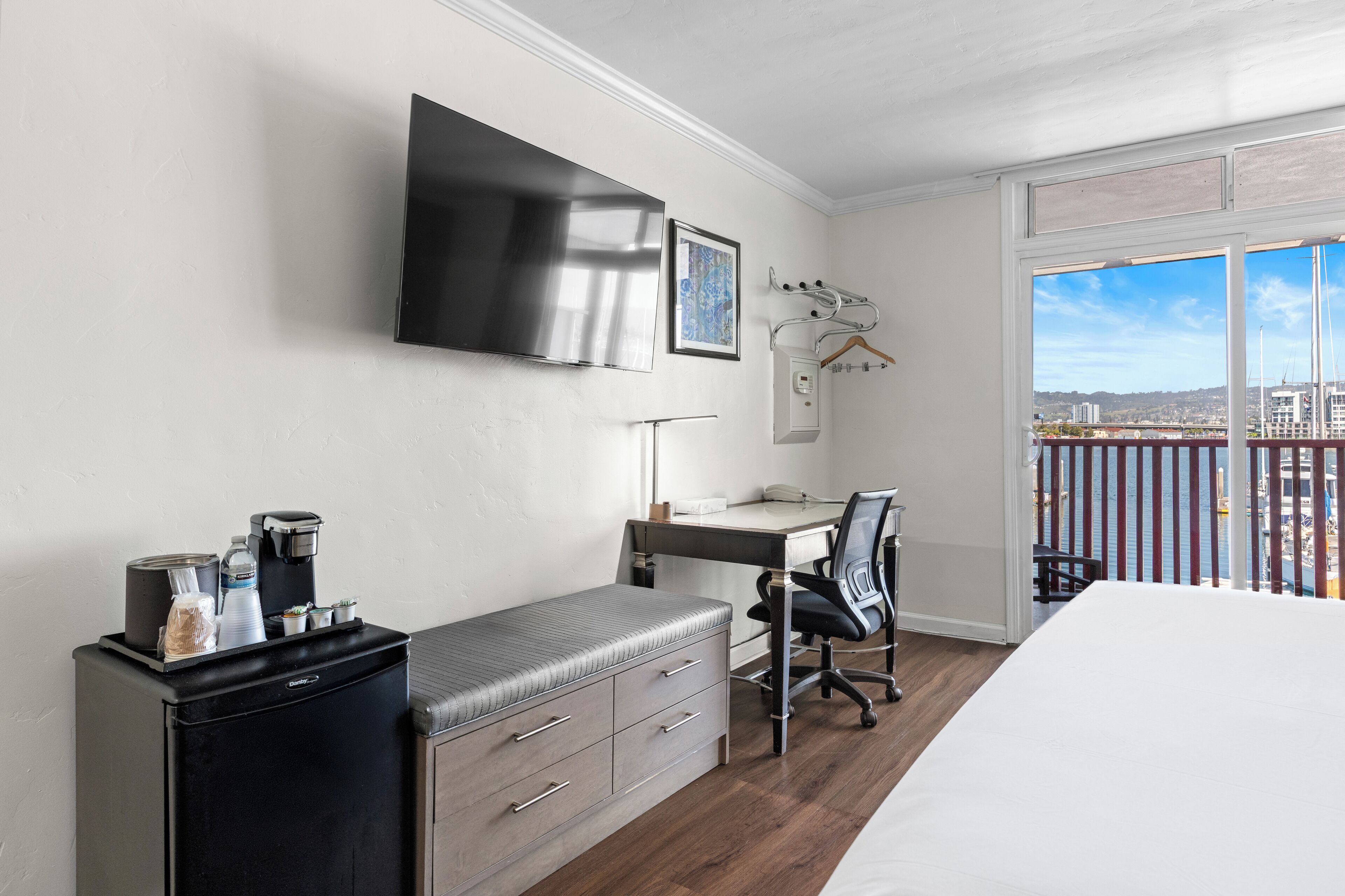A hotel room with a bed, a desk, a chair, a TV, a coffee machine, and a view of the city.