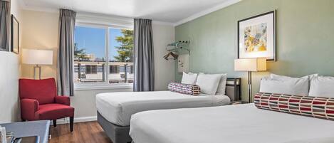 Une chambre d’hôtel avec deux lits, un fauteuil rouge, un bureau avec une lampe et une fenêtre avec des rideaux.