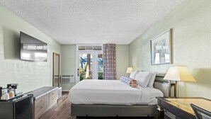 Habitación de hotel con cama, escritorio, silla y televisor montado en la pared.