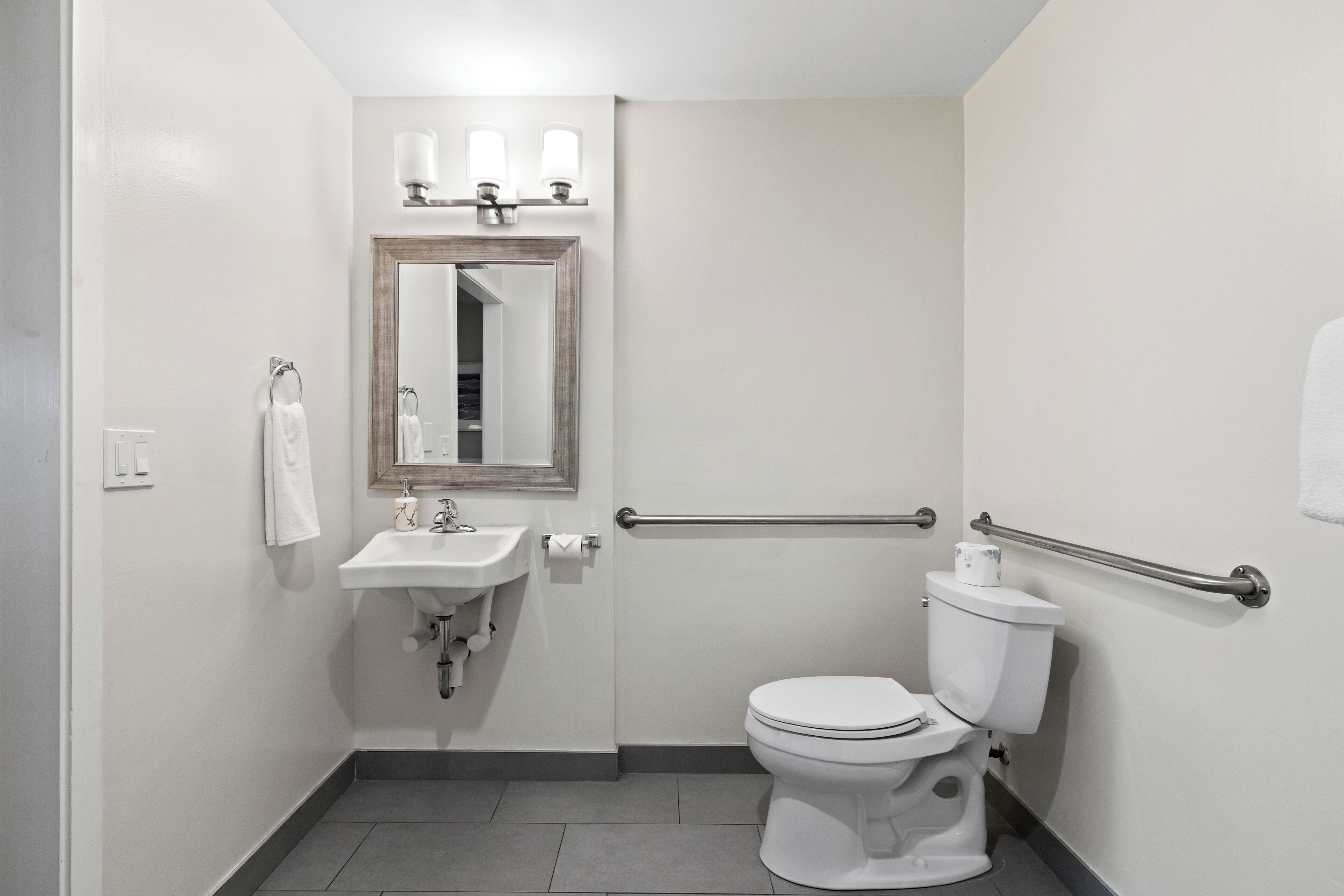 A small, modern bathroom with a white sink, mirror, and toilet.