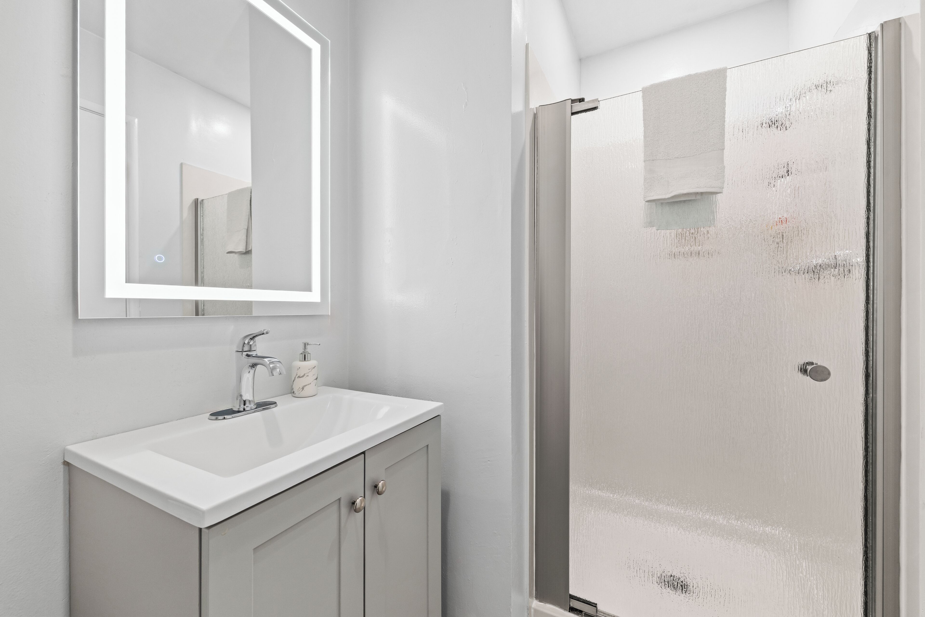 Un baño con lavamanos blanco, un espejo y cabina de ducha de vidrio.