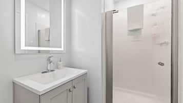 Un baño con lavamanos blanco, un espejo y cabina de ducha de vidrio.