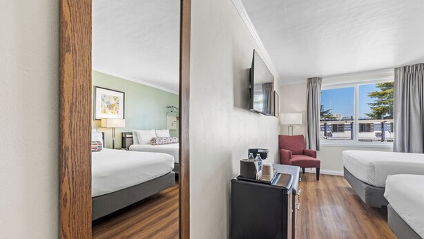 Quarto de hotel com duas camas, uma escrivaninha, uma cadeira, uma televisão e uma janela grande com cortinas.