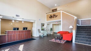 A hotel reception area with a wooden reception desk, a seating area with patterned chairs, and a staircase leading to an upper level. - Quality Inn & Suites Heritage Park (Kissimmee)