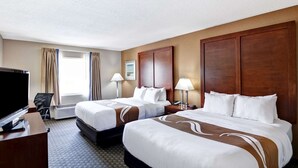 A hotel room with two beds, a desk with a TV, a chair, and a window with curtains. - Quality Inn & Suites Heritage Park (Kissimmee)