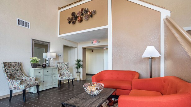 A living room with patterned chairs, a red sofa, a wooden coffee table, and a decorative wall piece. - Quality Inn & Suites Heritage Park (Kissimmee)