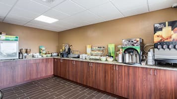 A self-service breakfast bar with various food and beverage options, including a coffee machine and a fruit juice dispenser.