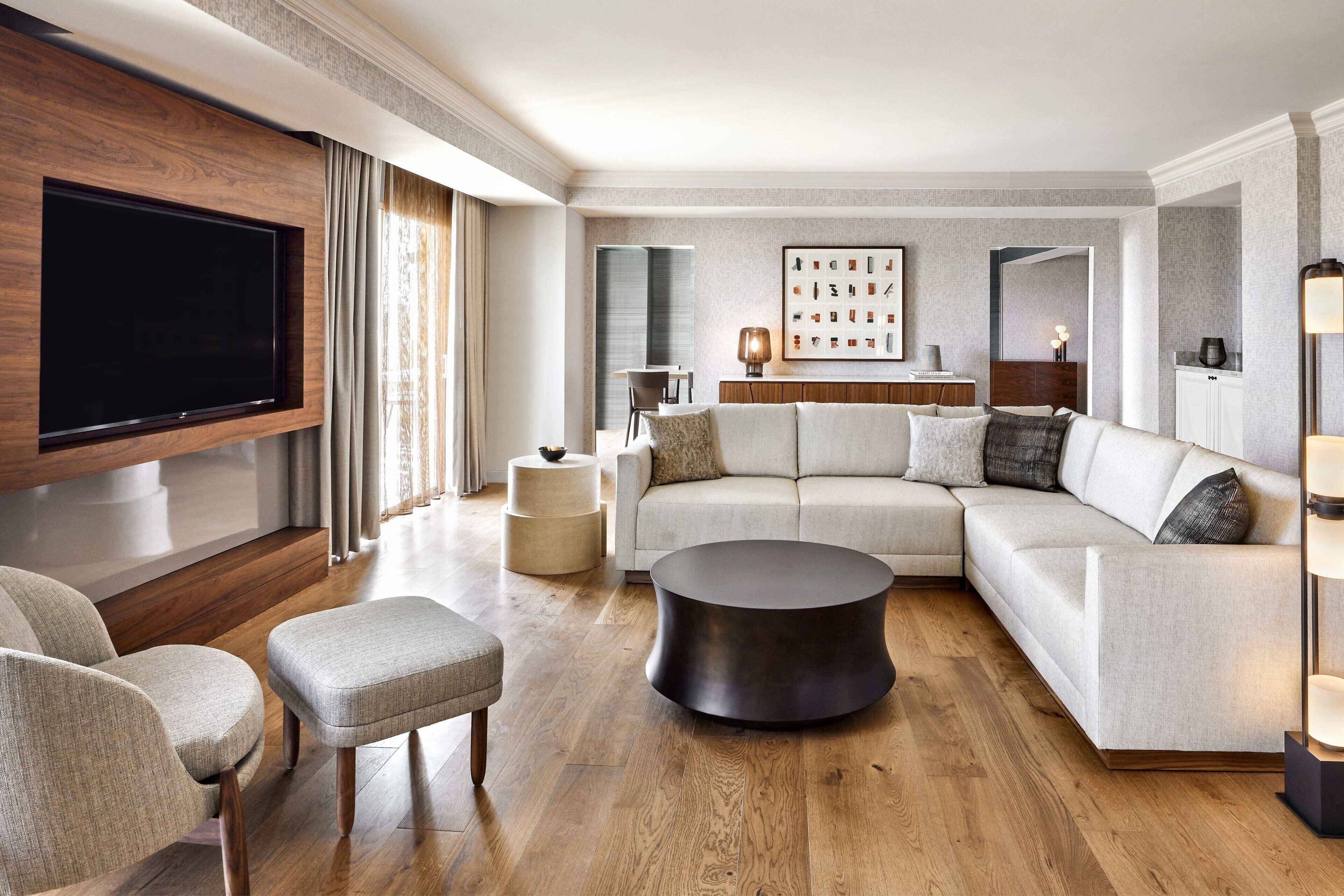 A modern living room with a large flat-screen TV, a sectional sofa, a round coffee table, and a sideboard.