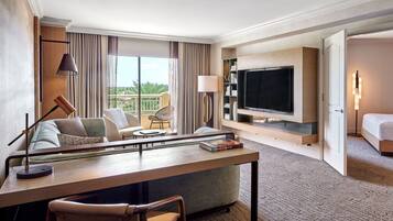 A hotel room with a flat-screen TV, a sofa, a dining table, and a balcony with a view.