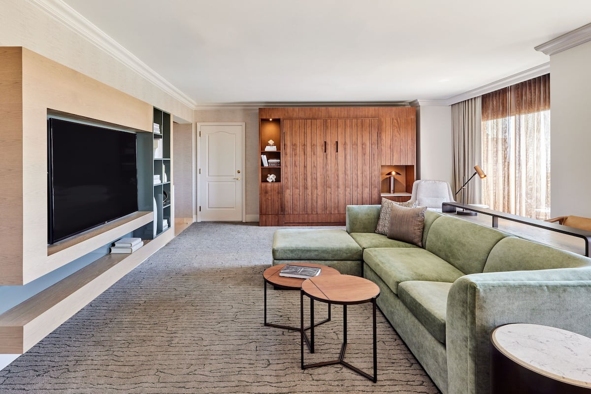 A modern living room with a flat-screen TV, green sofa, two side tables, and a wooden cabinet.
