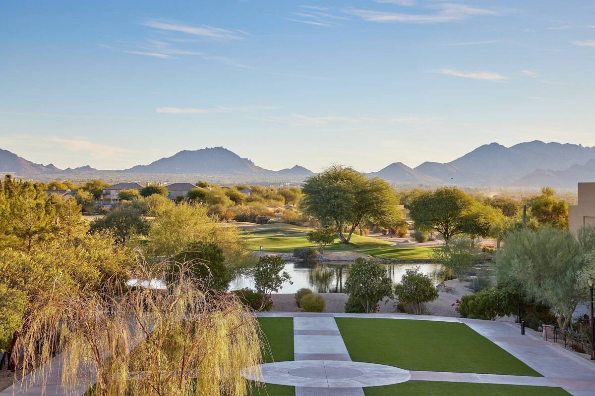 A golf course with a pond, surrounded by trees and mountains.