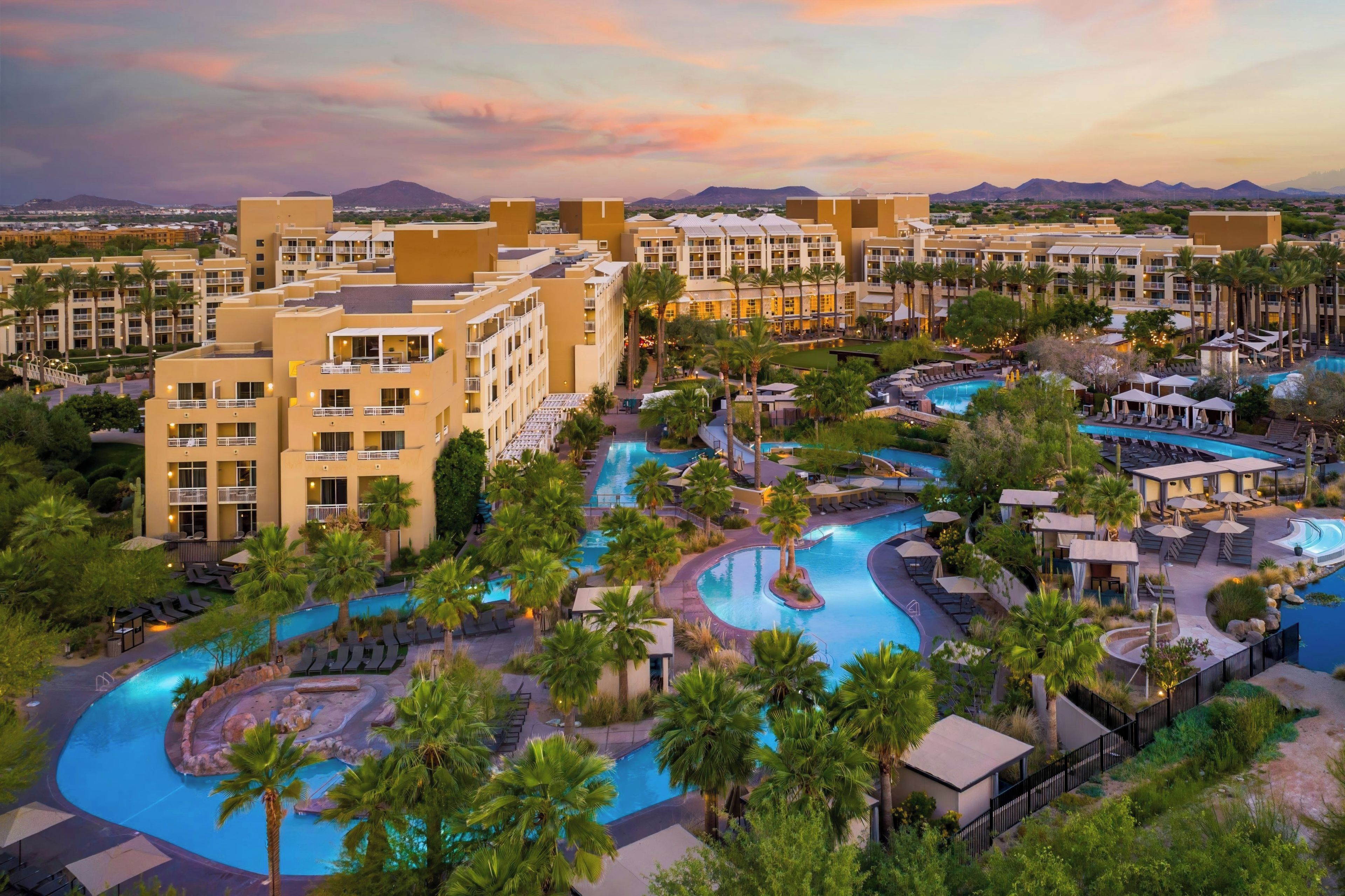 A resort with multiple swimming pools, palm trees, and a mountainous backdrop.