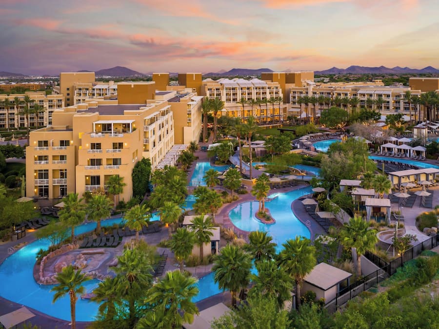 A resort with multiple swimming pools, palm trees, and a mountainous backdrop.