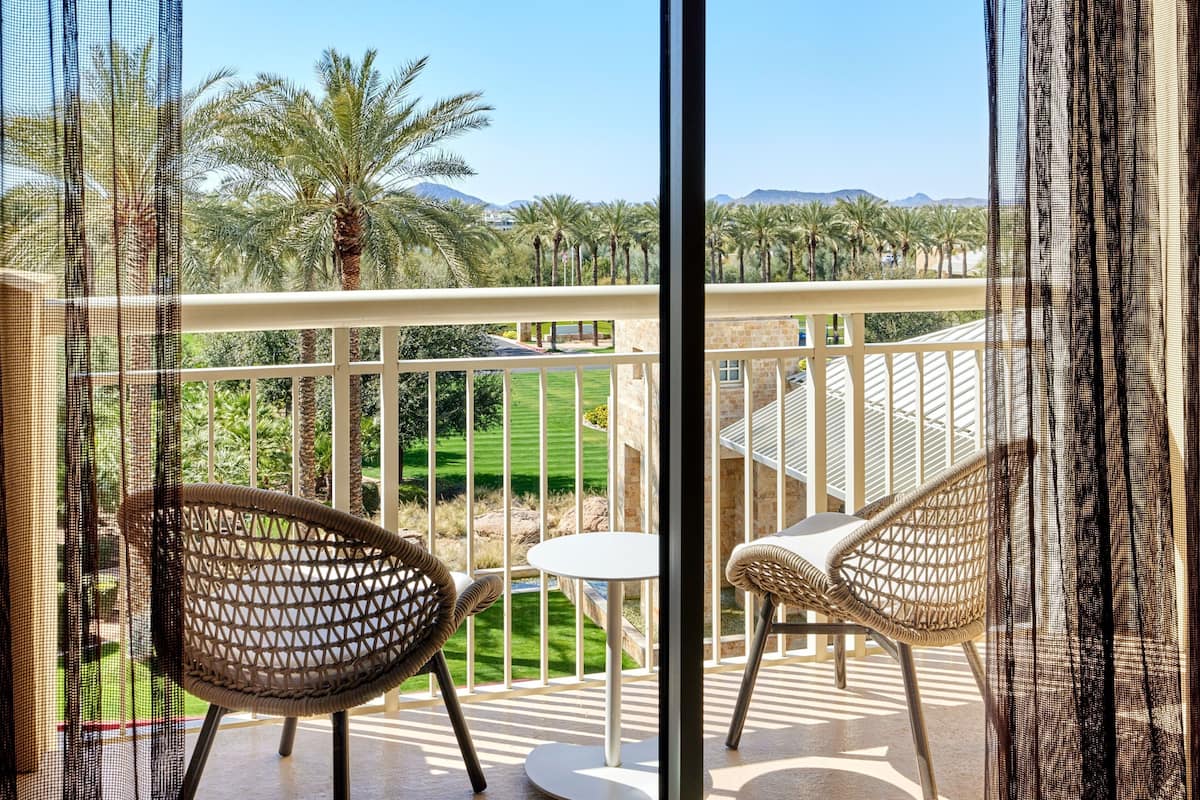 A balcony with wicker chairs and a small table, overlooking a well-manicured lawn and palm trees.
