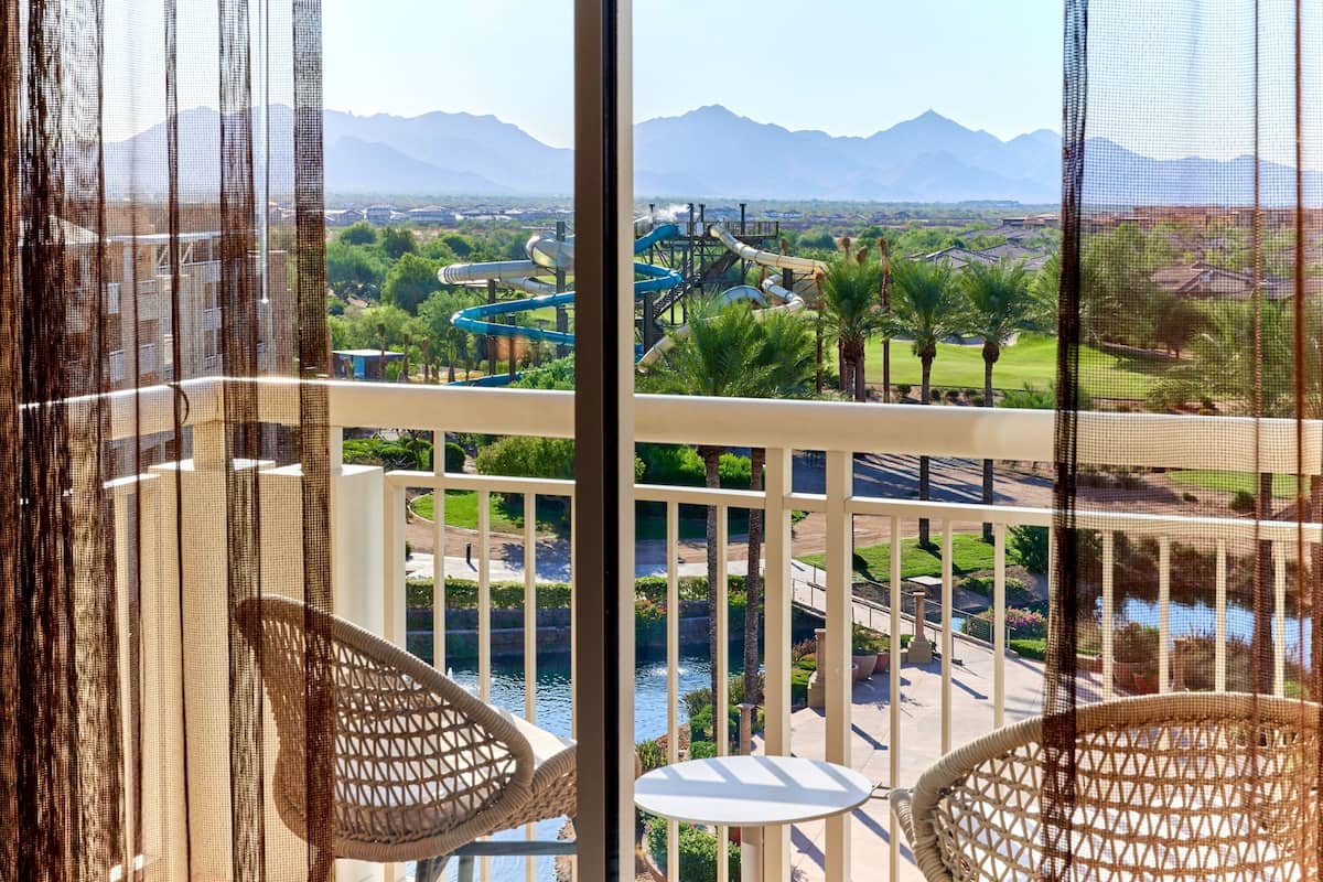 A balcony with wicker chairs and a table, overlooking a water park with slides and a river.