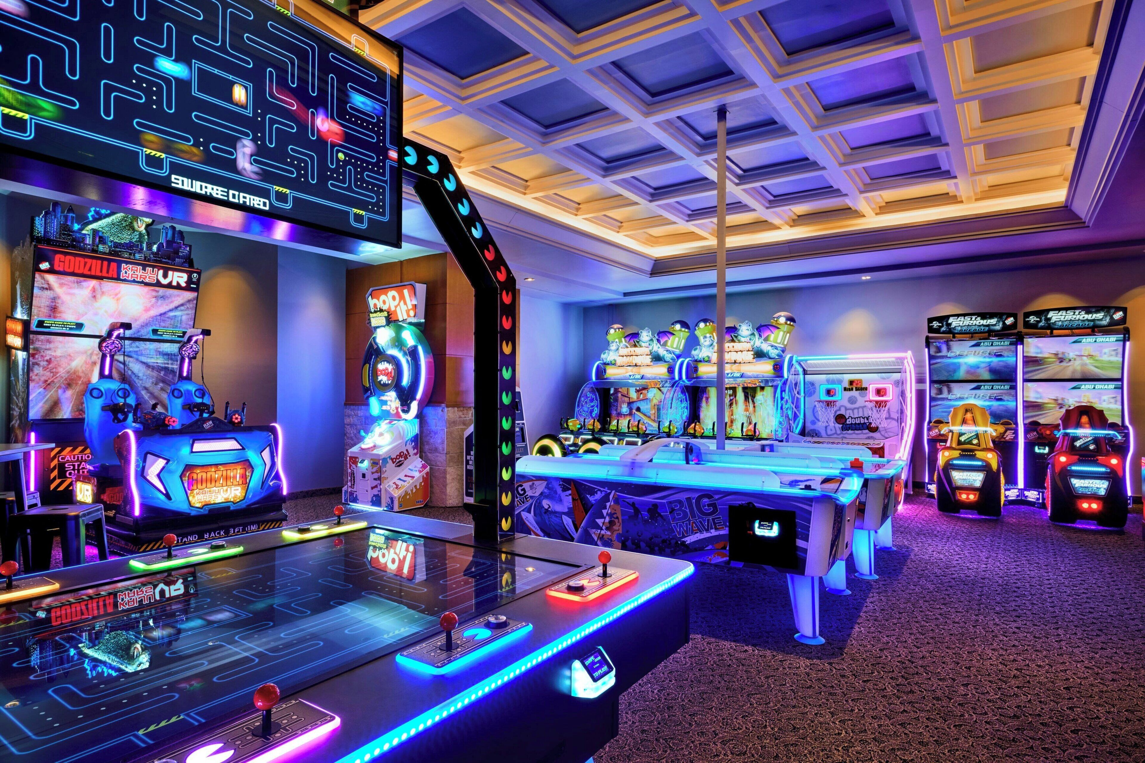 Een speelhal met verschillende machines, waaronder een spel met het thema 'Godzilla' en een 'Big Wave' spel.