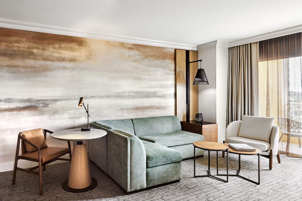 A modern hotel room with a sectional sofa, a round coffee table, a chair, and a lamp.